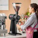 A woman in a pink apron using a Mahlkonig coffee grinder.