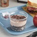 A plastic cup of Our Specialty Treat Shop Chocolate Tres Leches Cake on a tray with a sandwich and an apple.