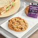 An individually wrapped oatmeal raisin cookie on a tray with a sandwich and a bag of chips.