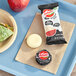 A brown tray with a sandwich, apple, and a round white Babybel cheese on it with a black wrapper.