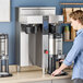 A man standing next to a Fetco twin automatic coffee machine with two black containers.