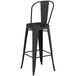 A Lancaster Table & Seating black metal bar stool with a backrest on a table.