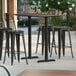 A Lancaster Table & Seating rectangular table with 4 black metal barstools on a patio.