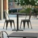 A Lancaster Table & Seating black metal table and two chairs on an outdoor patio.