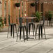 A Lancaster Table & Seating Excalibur Yukon Oak bar height table with four black chairs on a patio.