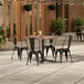 A Lancaster Table & Seating Excalibur textured Yukon Oak table with black chairs on an outdoor patio.