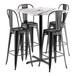 A Lancaster Table & Seating bar height table with a white marble top and four black outdoor bar stools.