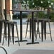 A Lancaster Table & Seating rectangular bar height table with black metal chairs on a patio.