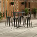 A Lancaster Table and Seating bar height table with two chairs on an outdoor patio.