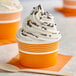 An orange and white paper cup filled with frozen yogurt.