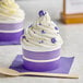 A close up of a purple and white striped cupcake in a purple paper cup with a wooden spoon.