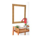 A BrandtWorks wooden mirror with a brushed gold finish on a table with a plant and picture frame.