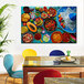 Mexican cuisine canvas wall art on a blue wall above a table with Mexican food on it and red and blue chairs.