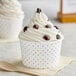 A Choice polka dot paper food cup filled with ice cream with white frosting and colorful dots.