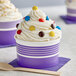 A purple and white paper cup with a scoop of ice cream and candy on top.