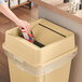 A hand using a red box to open a Lavex beige square trash can.