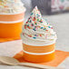 A Choice orange paper frozen yogurt cup filled with ice cream and sprinkles.