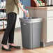 A woman putting a bag in a Lavex gray plastic trash can.