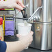 A hand pouring coffee from a Grindmaster coffee shuttle into a cup.