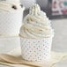 Two white polka dot paper cups filled with frozen yogurt topped with sprinkles.