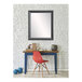 A BrandtWorks matte black mirror hanging on a white wall above a red chair with wooden legs.