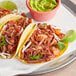A plate of two tacos with Chunk Foods Plant-Based Vegan Shredded Beef, limes, and guacamole.
