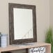 A BrandtWorks Rustic Urrutia distressed brown finish mirror on a wall above a shelf.