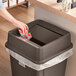 A woman putting a box in a brown square trash can with a swing lid.