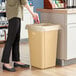 A person putting a bag into a Lavex beige square trash can in a corporate office cafeteria.