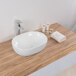 A white Ruvati oval ceramic sink on a wood counter.