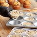 A person in black gloves holding a muffin tin with chocolate chip muffins.