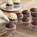 A person using a pastry bag to frost a chocolate cupcake.