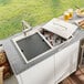 A Ruvati stainless steel outdoor ice chest and sink with a sink cover on a counter.