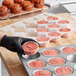 A person in gloves putting Brill strawberry muffin batter into a muffin tin.