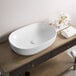 A Ruvati white vitreous porcelain oval vessel sink on a wood table.