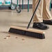 A person sweeping the floor with a Lavex 24" wood push broom head.