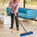 A woman using a Lavex push broom with unflagged bristles and a metal handle to sweep the floor.