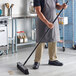 A man sweeping the floor with a Lavex 24" polypropylene push broom with unflagged bristles and a metal handle.