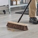 A person sweeping the floor with a Lavex wood broom head.