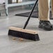 A person sweeping the floor with a Lavex wood push broom.