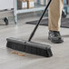 A person sweeping the floor with a Lavex polypropylene push broom head.