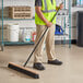 A man in a safety vest sweeping the floor with a Lavex wood push broom.