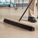 A person using a Lavex wood push broom to sweep a grocery store aisle.