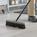 A person sweeping the floor with a Lavex polypropylene push broom head.