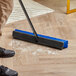 A person using a Lavex push broom with unflagged bristles to clean the floor.