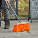 A person sweeping the sidewalk with a Lavex Heavy-Duty Wood Street Broom.