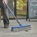 A person sweeping the sidewalk with a Lavex blue push broom.