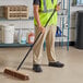 A man in a safety vest using a Lavex wood push broom with palmyra bristles.