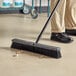 A person sweeping the floor with a Lavex push broom.