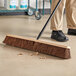 A person sweeping the floor with a Lavex wood push broom head.